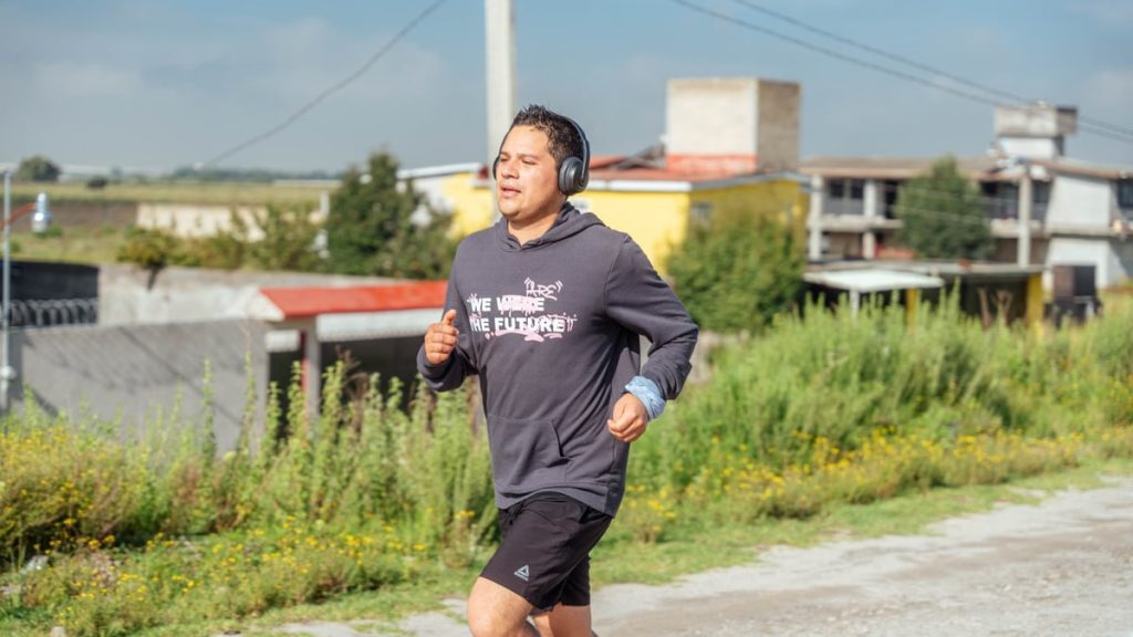 A man runs outdoors listening to music, showcasing rural surroundings and focus on fitness.