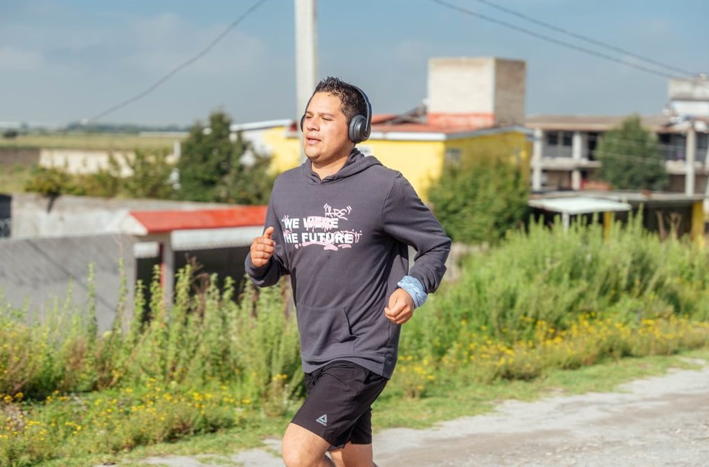 A man runs outdoors listening to music, showcasing rural surroundings and focus on fitness.